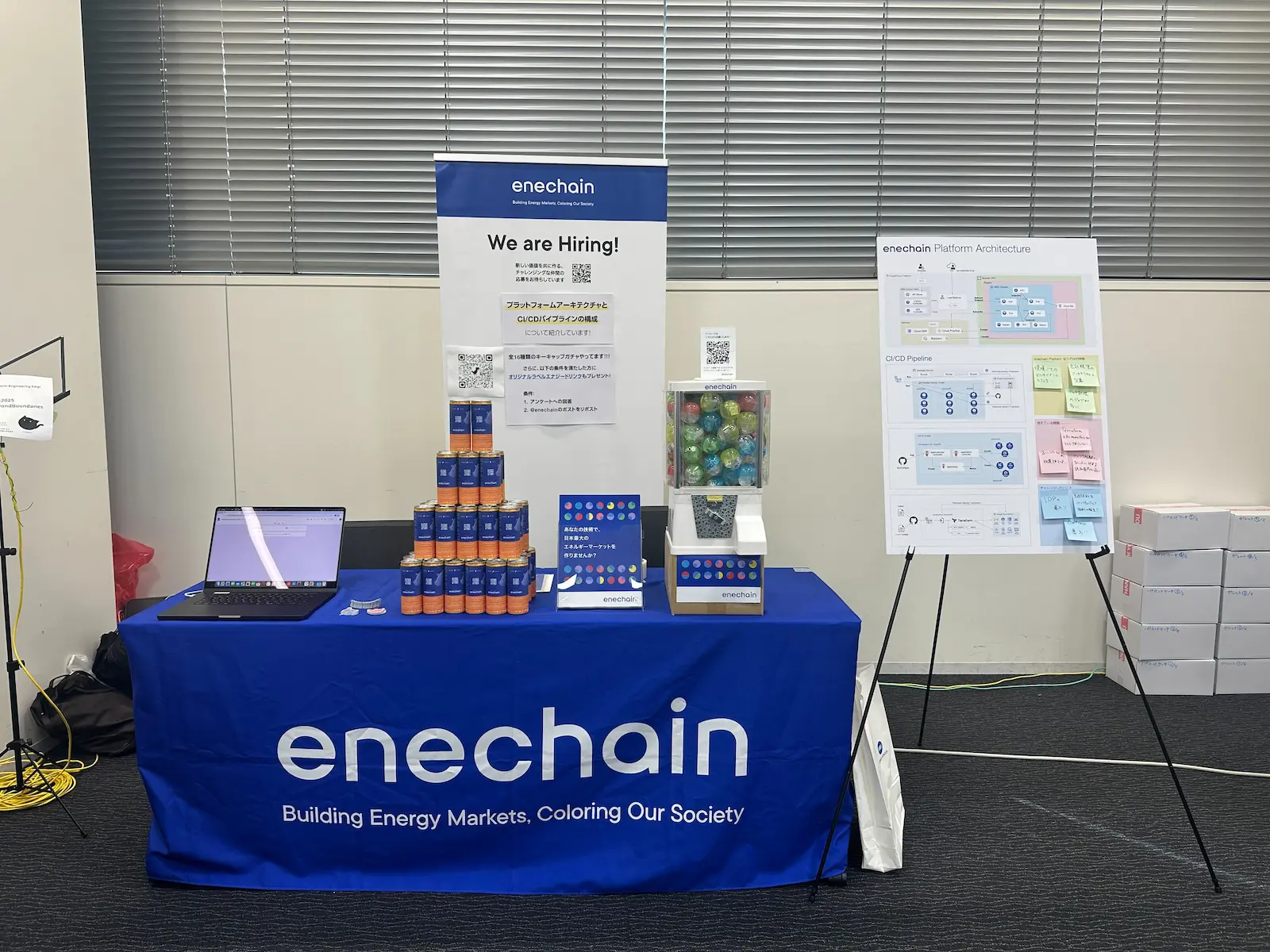 技術カンファレンスにおけるenechain社のブース全体の様子。「We are Hiring!」のポスターと共に28 BLACKオリジナルラベルエナジードリンクがブース前面に展示され、来場者を惹きつける演出がされている