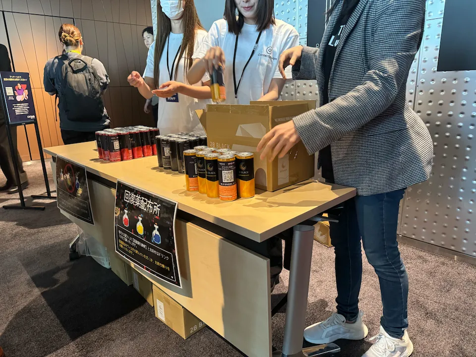 CX Circle Tokyo 2024の会場内で、スタッフが28 BLACKオリジナルラベルを回復アイテムとして参加者に配布している様子