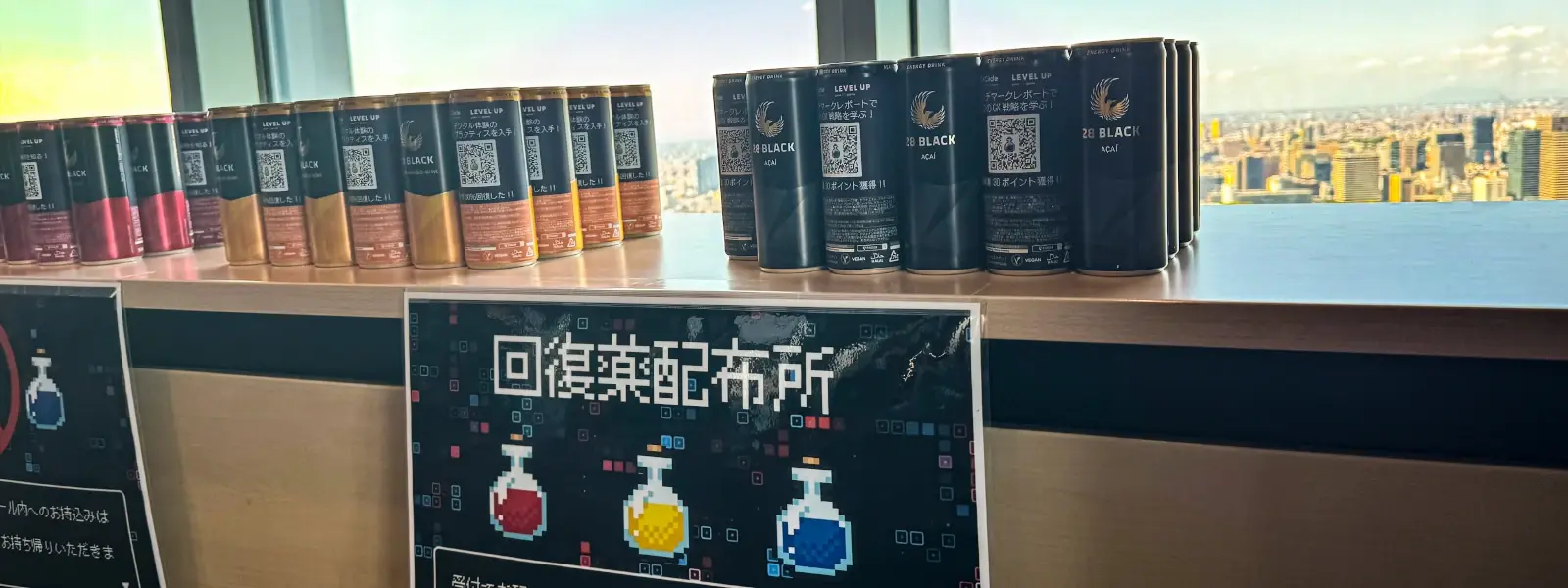 CX Circle Tokyo 2024イベント会場で「回復薬配布所」の看板とともに展示された28 BLACKオリジナルラベルエナジードリンク。RPGのポーション風デザインで、複数のフレーバーが並んでいる