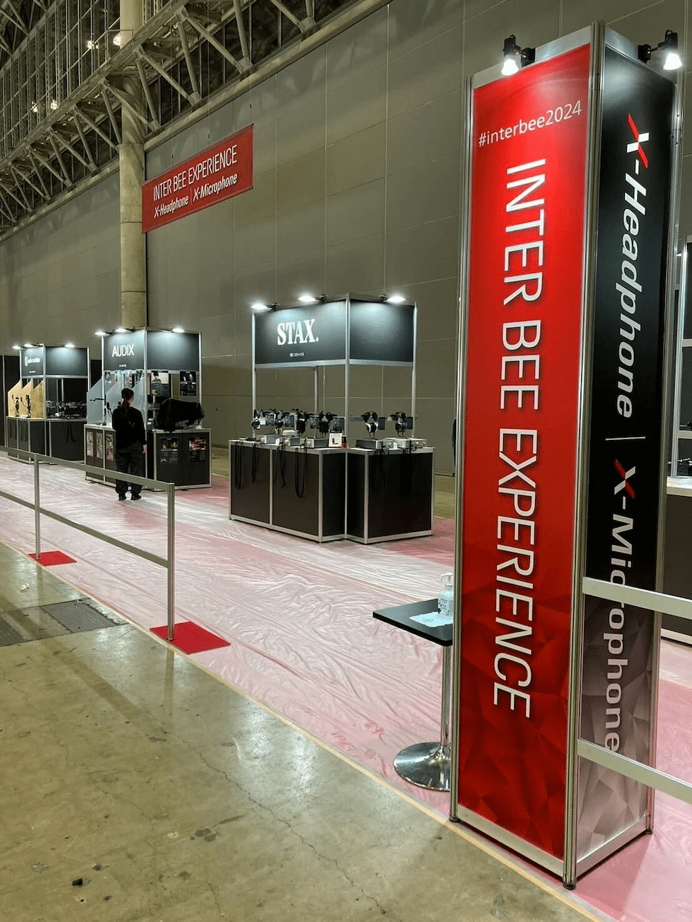 Inter BEE 2024の「INTER BEE EXPERIENCE」エリアにあるSTAX社のブース全景。「#interbee2024」のサイネージが掲示され、複数のヘッドホンが試聴用に展示されている