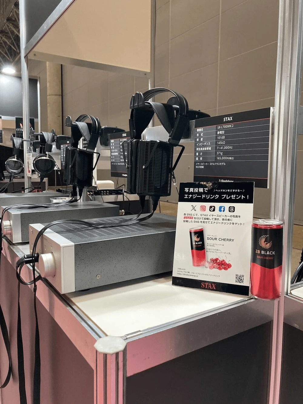 Inter BEE 2024におけるSTAX社の展示ブース。複数の静電型ヘッドホンが展示され、来場者が試聴できるようになっている。ブース内に28 BLACKオリジナルラベルエナジードリンクと写真投稿キャンペーンの案内が設置されている